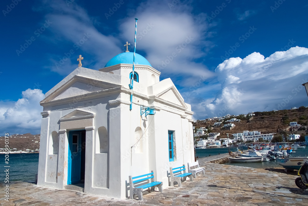 Agios Nikolaos church in Mykonos, Greece. Temple building with blue dome on sea quay. Church on sunny seaside. Summer vacation on mediterranean island. Wanderlust and travelling concept Agios Nikolaos church in Mykonos, Greece. Temple building with blue dome on sea quay. Church on sunny seaside. Summer vacation on mediterranean island. Wanderlust and travelling concept