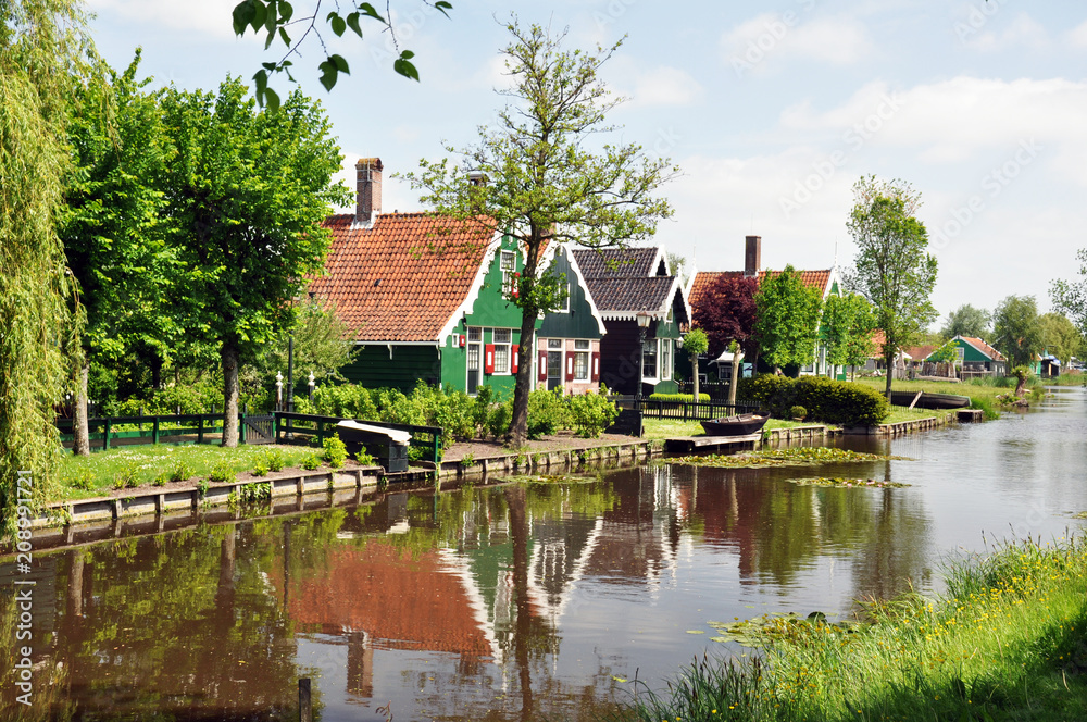 Landscape of the village in the Netherlands. The wooden houses are colourful and set along a picturesque lake surrounded by trees .