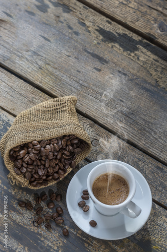 white cup of steamingcoffee and sackwith beans on table, view from above photo