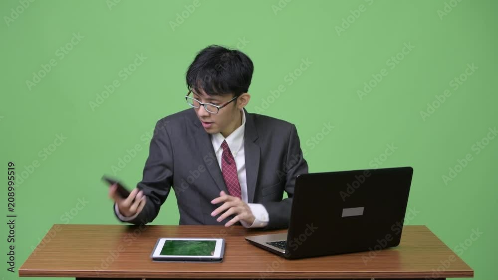 Young happy Asian businessman video calling with phone while working Young happy Asian businessman video calling with phone while working