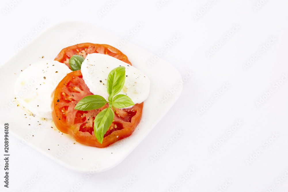 Mozzarella and tomatoes with basil on a white square plate. The background is white. Copiespice. Mozzarella and tomatoes with basil on a white square plate. The background is white. Copiespice.