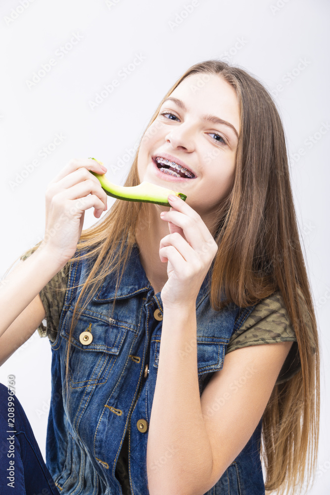 Dental Health Concepts. Smiling Positive Caucasian Teenage Girl With Teeth Braces Eating Slice of Avocado.Posing Against White. Dental Health Concepts. Smiling Positive Caucasian Teenage Girl With Teeth Braces Eating Slice of Avocado.Posing Against White.