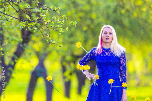 Beauty and Fun Concepts. Smiling Positive Caucasian Blond Girl in Front of Falling Bunch of Daffodils Away. Posing Against Nature Background. photo