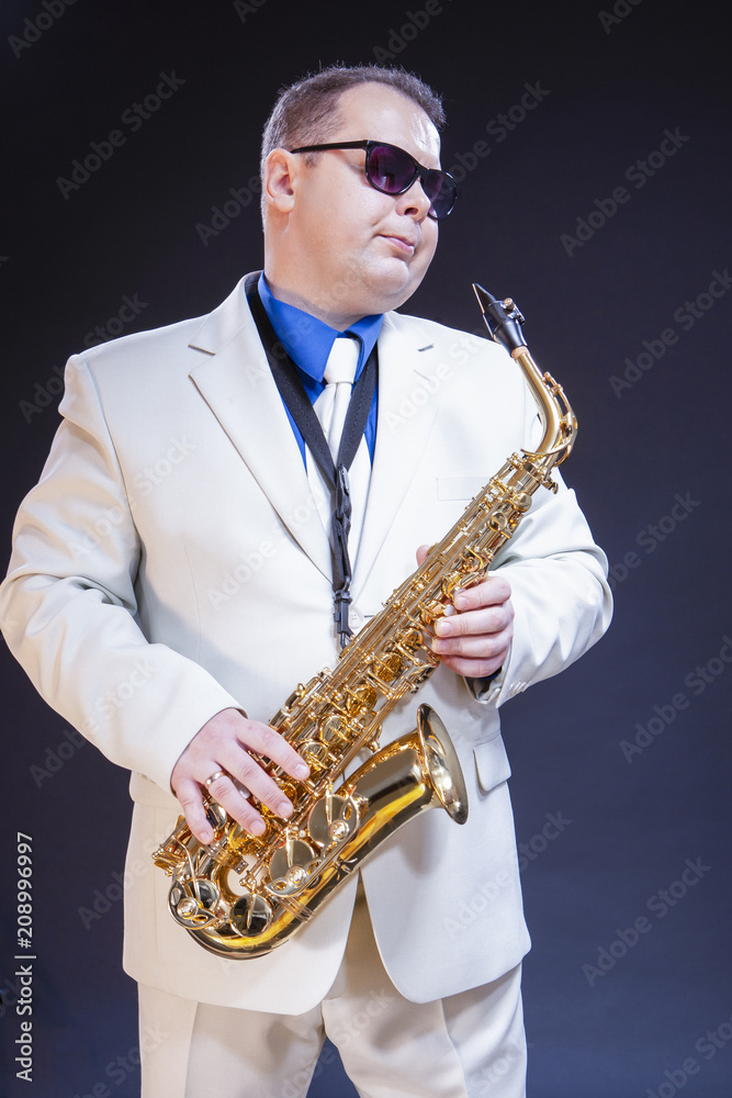 Fototapeta premium Dreaming Male Saxophonist Posing In Sunglasses With Sax. Against Black Background.
