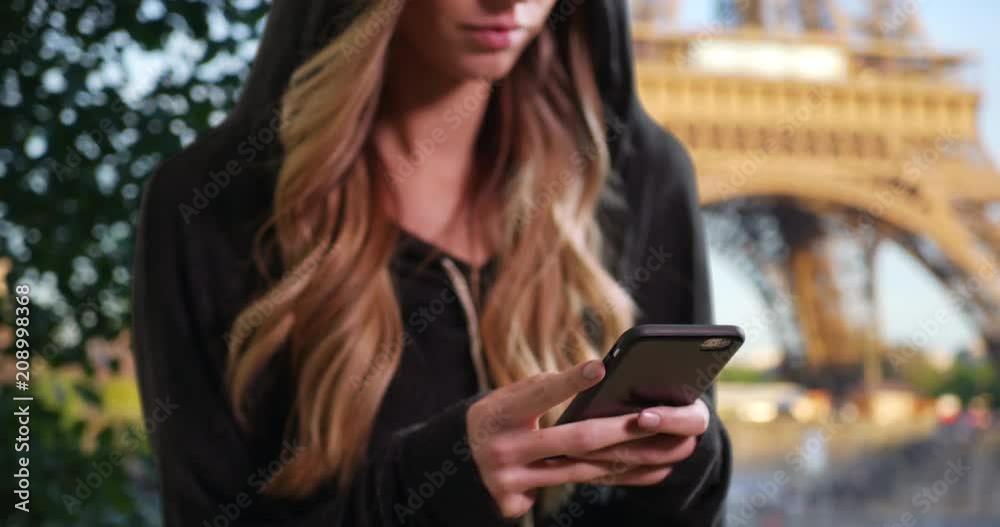 Blonde female in a hoodie texting with cellphone in Paris, Caucasian woman using mobile phone outside with Eiffel Tower in the background, 4k Blonde female in a hoodie texting with cellphone in Paris, Caucasian woman using mobile phone outside with Eiffel Tower in the background, 4k