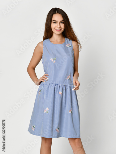 Young beautiful woman posing in new blue stripes casual summer dress on grey 