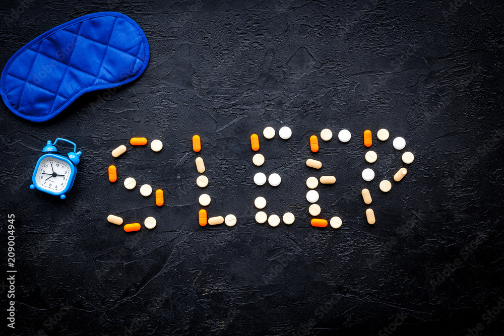 Obraz premium Medicine helps get asleep. Good sleep. Word sleep lined with sleeping pills near sleeping mask and alarm clock on black background top view copy space