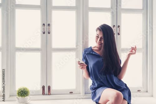Happy woman using mobile phone sit on windowsill