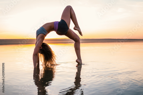 woman on the beach at sunset doing yoga asana. Morning natural stretch warm-up training