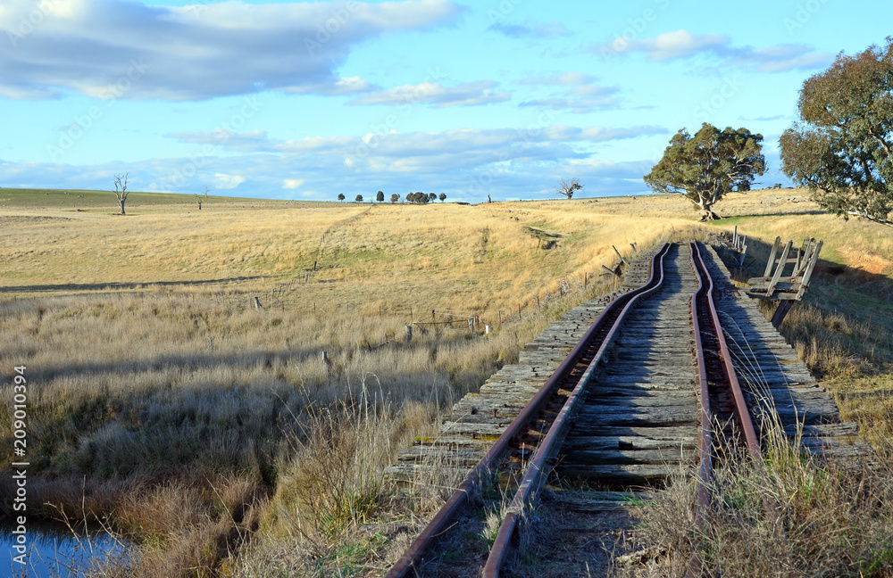 Old abandoned crooked rusty railway tracks on historic bridge over the Boorowa River through rural central west NSW, Australia Old abandoned crooked rusty railway tracks on historic bridge over the Boorowa River through rural central west NSW, Australia