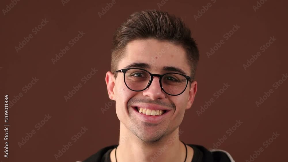 Portrait of happy laughing young guy with glasses on brown background. Portrait of young funny man with glasses smiling in front of camera.