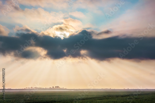 Rays of  sun browsing through a dark cloud over  wheat field during  sunrise. Summer landscape with a thunderstorm cloud_