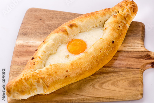 Delicious khachapuri with egg and cheese filling serving on wooden cutting board