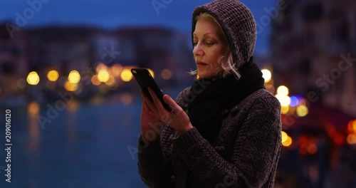 Older woman tourist using smartphone at night in venice during winter, Senior retiree travelling in Italy at night uses cell phone to check map app, 4k