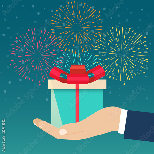 Hand holding blue gift box decorated against the background of fireworks. Vector flat illustration