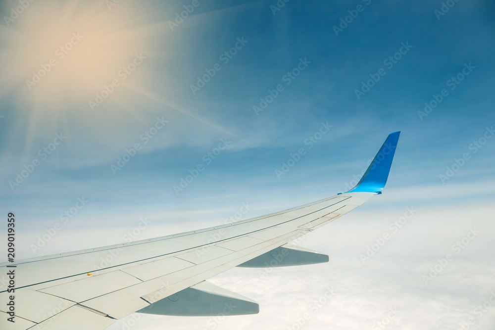 Obraz premium Wing of an airplane flying above the clouds on blue sky background