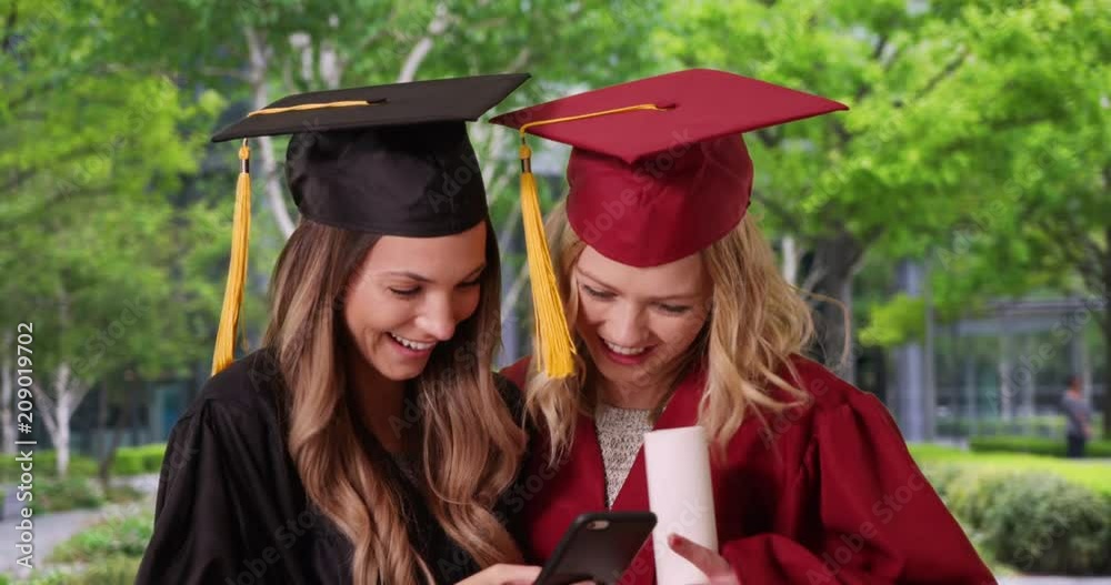 Couple of pretty white girls taking a selfie outside on their smartphone after their graduation, Attractive blonde and brunette in graduation gowns taking selfie outdoors, 4k Couple of pretty white girls taking a selfie outside on their smartphone after their graduation, Attractive blonde and brunette in graduation gowns taking selfie outdoors, 4k