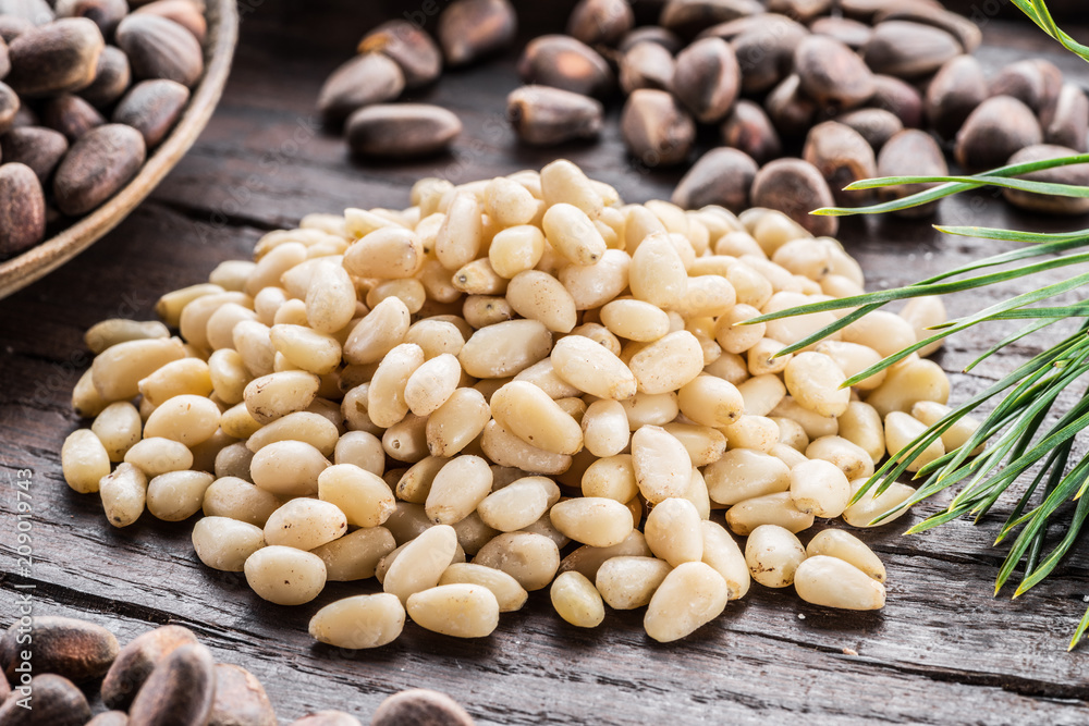 Fototapeta premium Pine nuts in the spoon and pine nut cone on the wooden table. Organic food.
