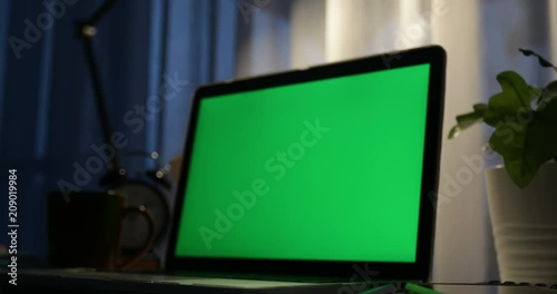 Laptop with green screen. Dark office. Dolly in . Perfect to put your own image or video.Green screen of technology being used. Chroma Key laptop
