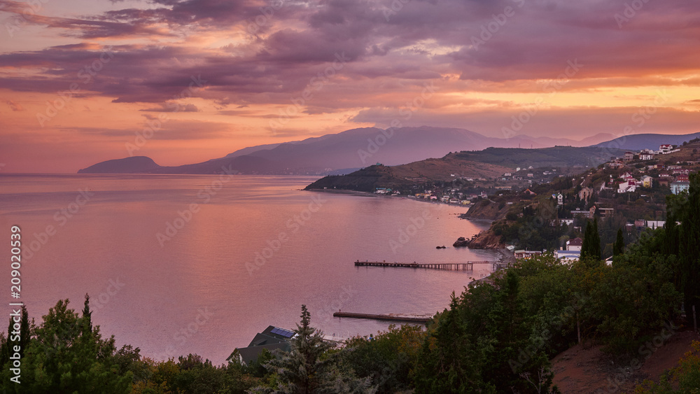Beautiful warm pink sunset on the Crimean coast. View of the village. Beautiful mountains on the horizon. Russia.