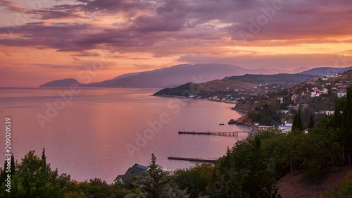 Beautiful warm pink sunset on the Crimean coast. View of the village. Beautiful mountains on the horizon. Russia.