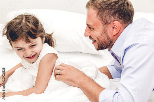 Father with little daughter having fun and playing together on the bed at home.Love of family and father day concept