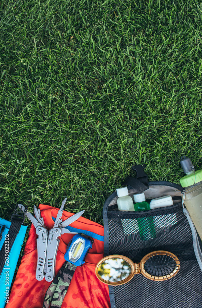Fototapeta premium Set of equipment for hiking and travel on green grass with copy space . Items include , multi tool, flashlight, hygiene products, tracking clothes, comb