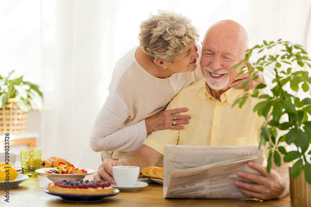 Smiling senior man reading newspaper while his wife kissing him