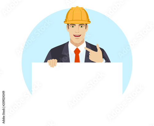 Businessman in construction helmet holding white blank poster and pointing at himself