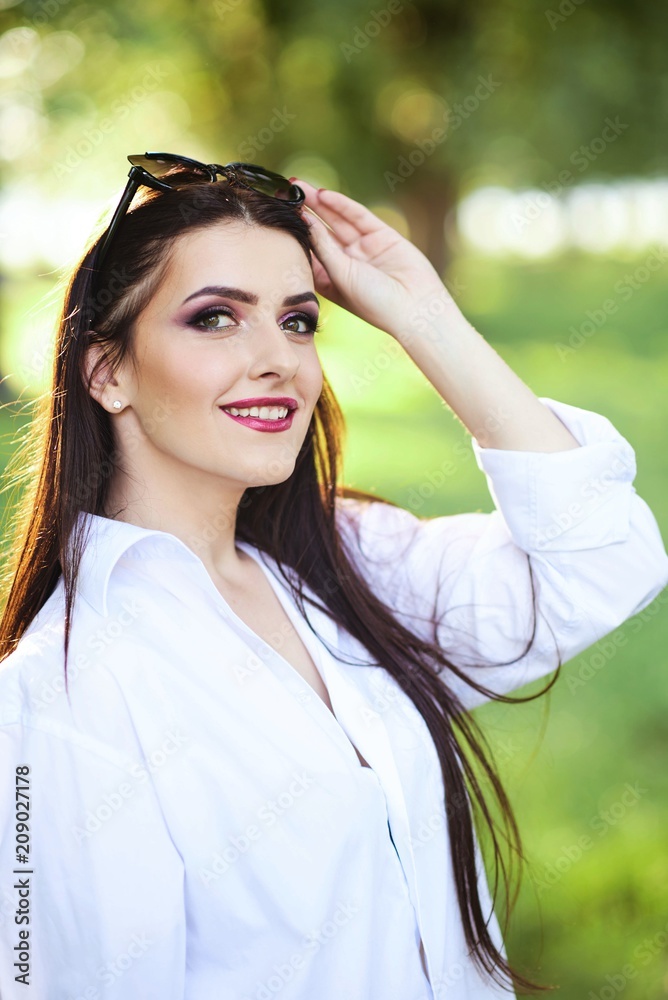 Cute young brunette girl with beautiful professional make-up on green background in park Cute young brunette girl with beautiful professional make-up on green background in park