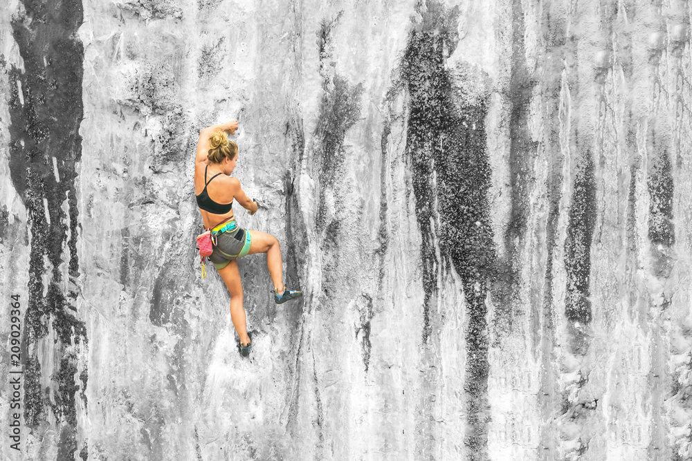Fototapeta premium Young woman climbing a cliff without safety equipment on a summer day, copy space