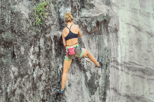 Young blonde woman climbing a cliff without safety equipment on a summer day