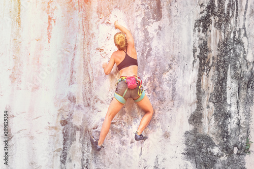Young woman climbing a cliff without safety equipment on a summer day. Toned
