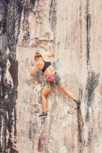 Young female rock climber climbing the cliff without safety equipment. Toned