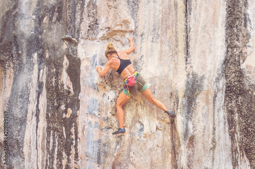 A young woman climber climbs the cliff