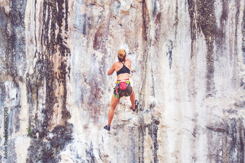 Young blonde woman climbing up a cliff without safety equipment. Adrenaline, strenght, ambition