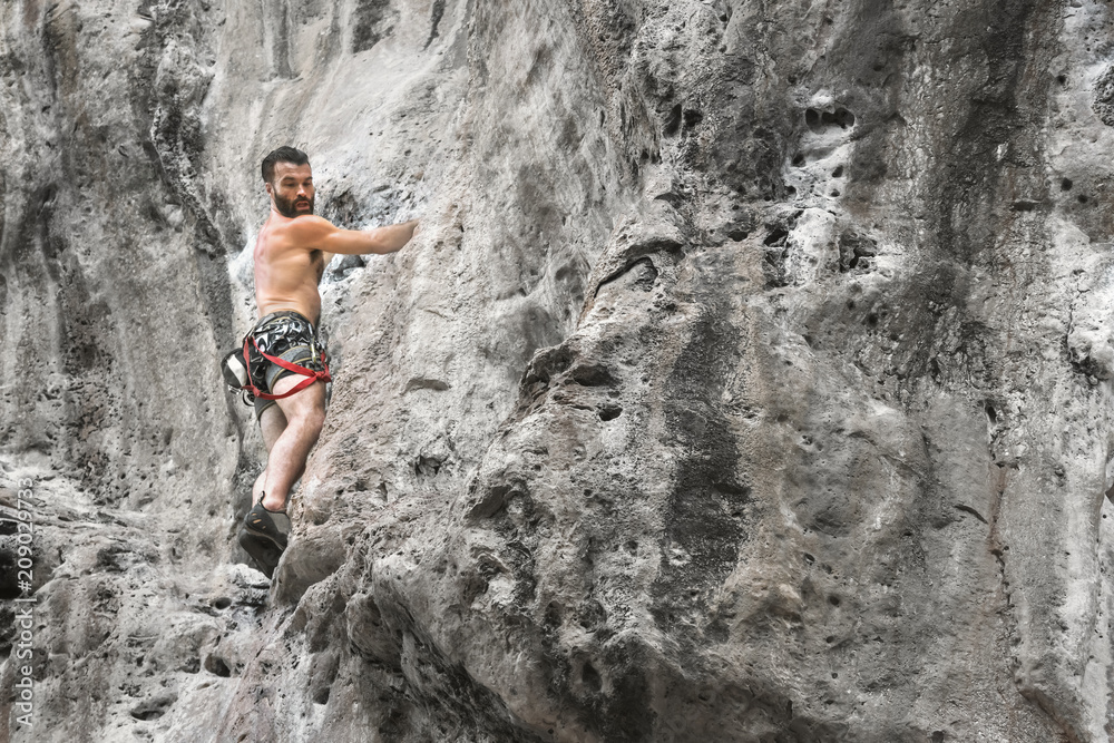 Young bearded male mountaineer standing on a ledge of a cliff and looking down, copy space