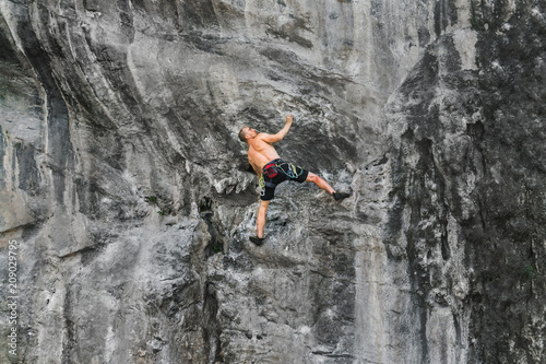 A young male athlete climbs up a cliff without a safety rope
