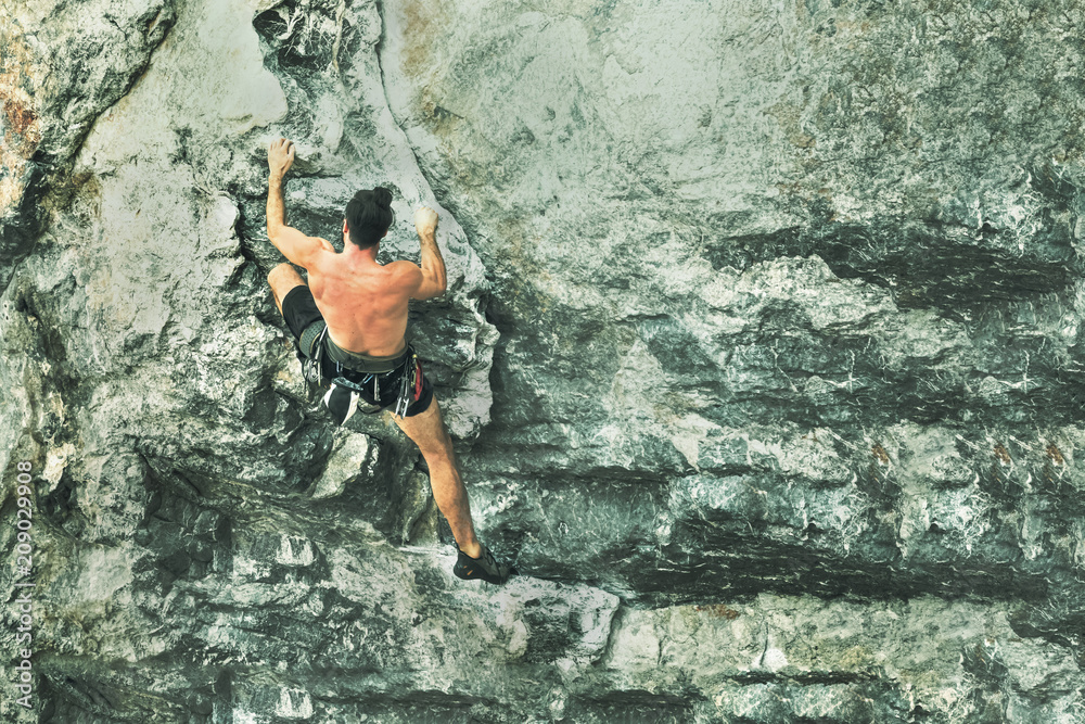 Young male climber climbing a rock wall without insurance equipment. Toned Young male climber climbing a rock wall without insurance equipment. Toned