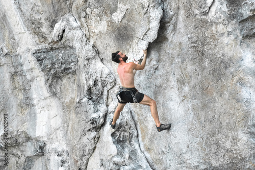 Young bearded man climbing a rock wall without safety rope