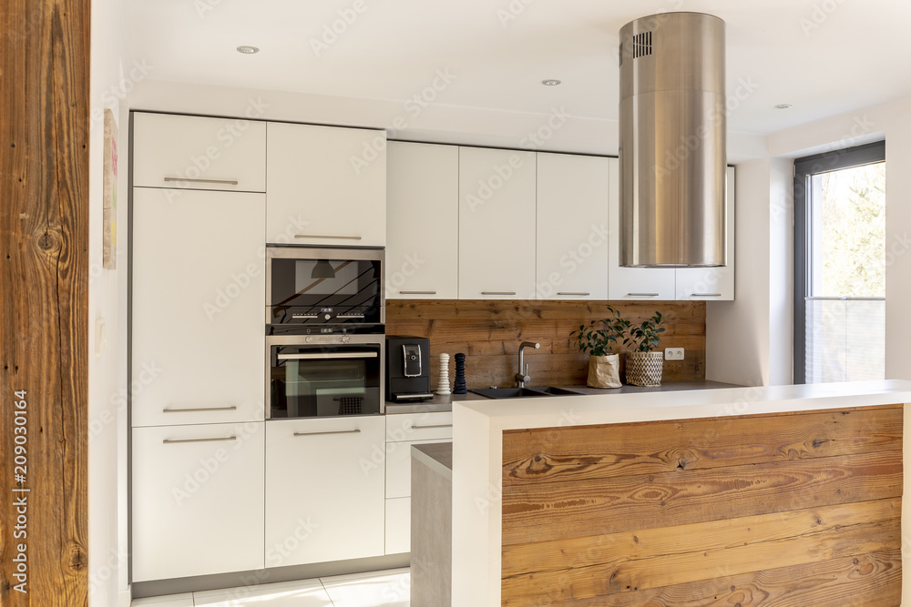 White modern kitchen interior with silver cooker hood above wooden countertop. Real photo White modern kitchen interior with silver cooker hood above wooden countertop. Real photo