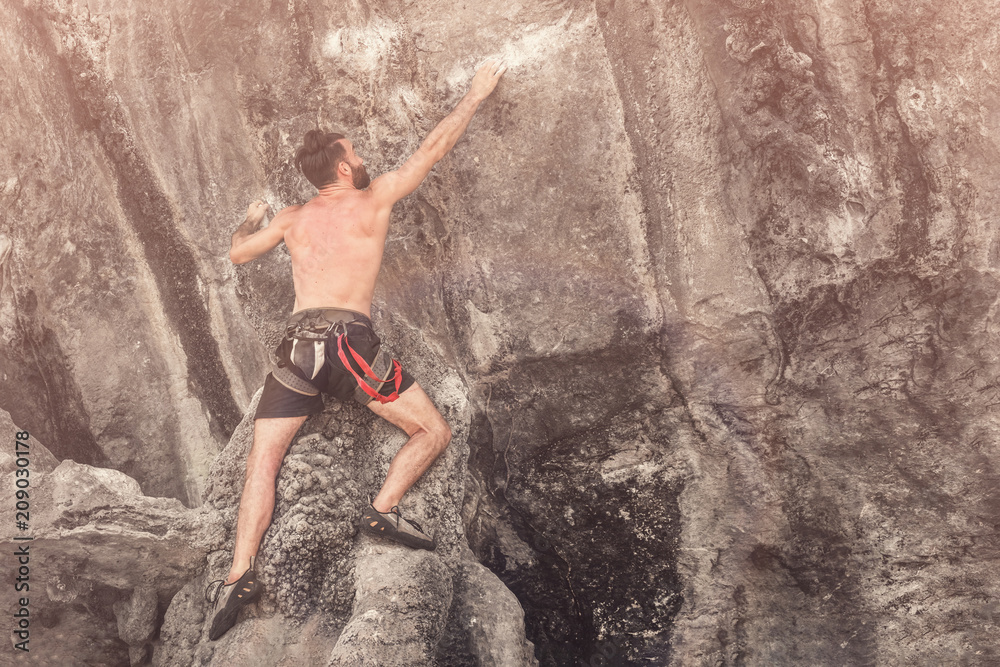 Young bearded man climbs the cliff without a safety rope. Toned Young bearded man climbs the cliff without a safety rope. Toned