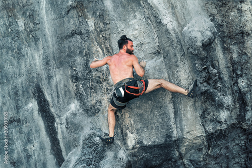 Young bearded male climber climbs a cliff without insurance