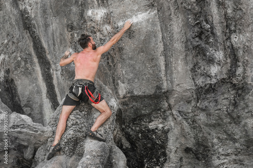 Young male mountaineer climbs on a rocky wall without rock-climbing equipment