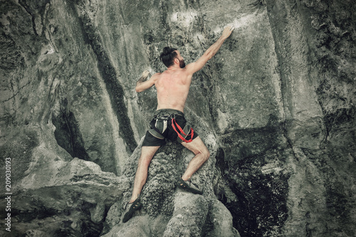 A young bearded man is climbing a rock without insurance. Toned