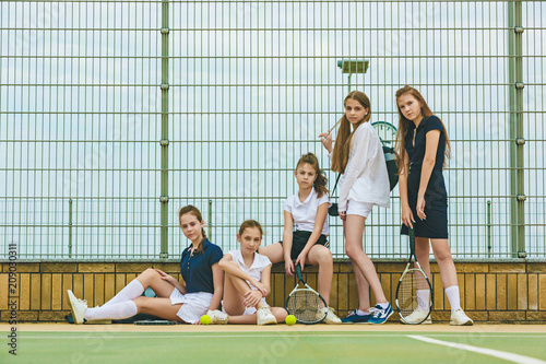 Portrait of group of girls as tennis players holding tennis racket against green grass of outdoor court © master1305