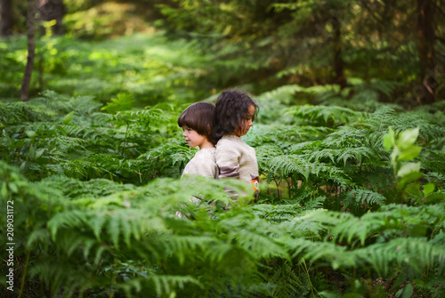 Two boys in identical sweaters are standing in the thickets of fern in the forest. Back to back.