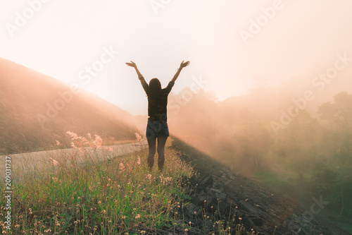 Back view of happy young woman raise arms with beautiful morning sunrise landscape, travel around the world concept.
