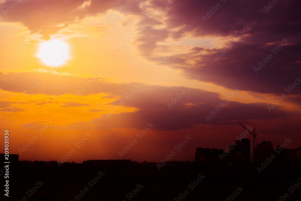 Magenta sunrise above silhouette of city buildings with tower cranes. Unusual cityscape with beautiful dawn. Picturesque warm city landscape with bright sunny sky. Big sun above city architecture.