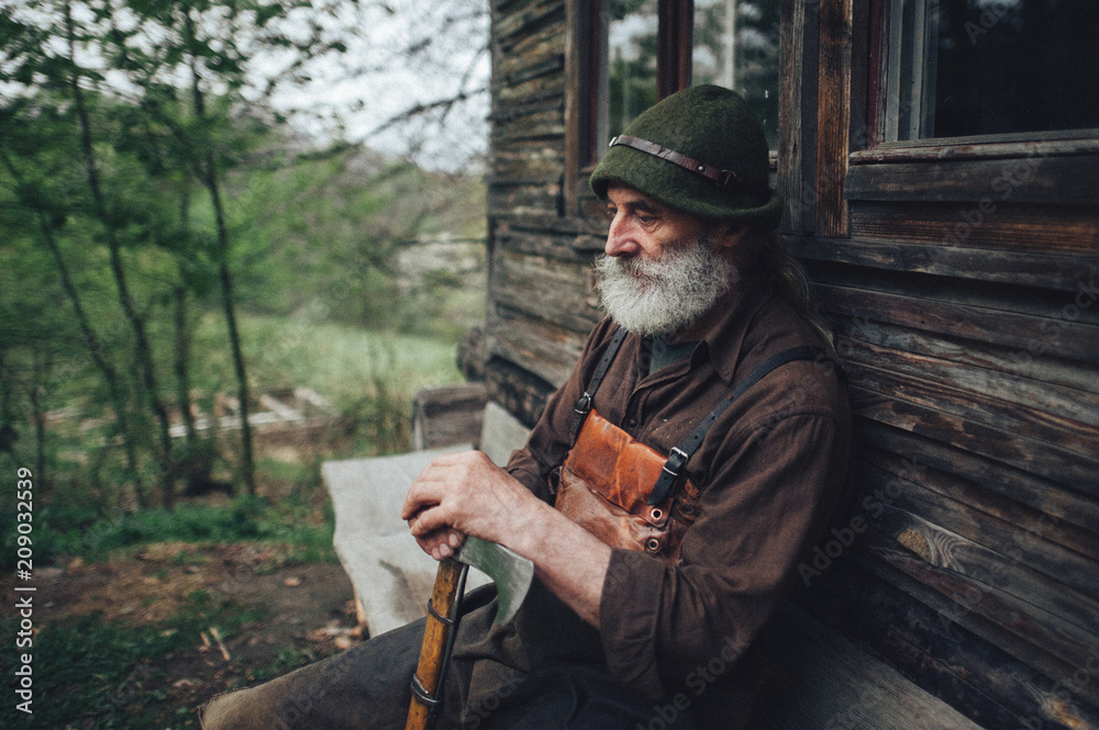 Naklejka premium old bearded forester with axe near wooden hut